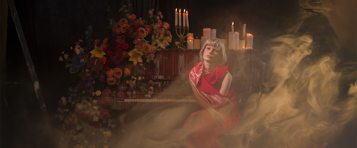 kobieta , w tle stylizowana sceneria, kwiaty, fortepian, świece i dym